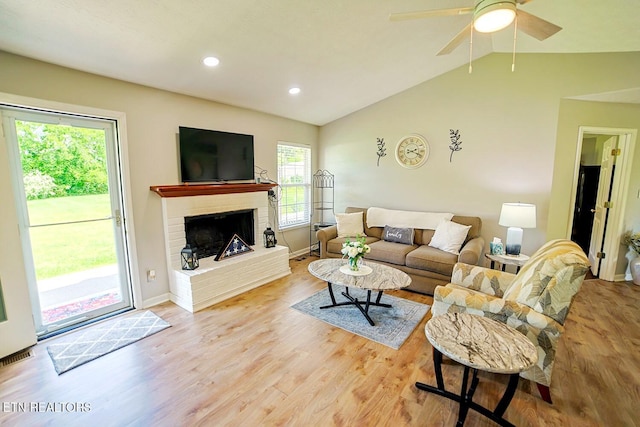 living room featuring lofted ceiling, light wood finished floors, a fireplace, baseboards, and a ceiling fan