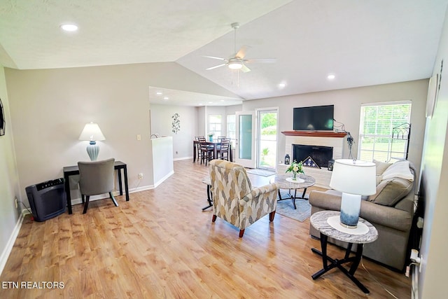living area with light wood finished floors, ceiling fan, vaulted ceiling, baseboards, and a fireplace