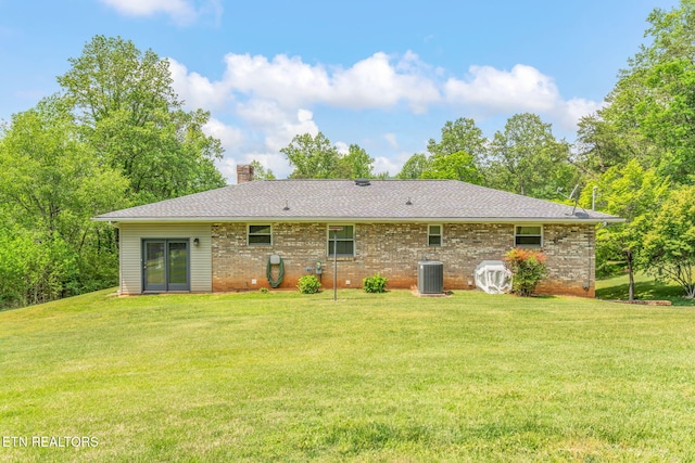 back of house with a chimney, central air condition unit, brick siding, a yard, and a shingled roof