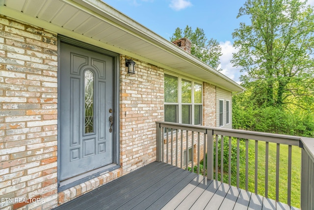 entrance to property featuring brick siding, a chimney, and a deck
