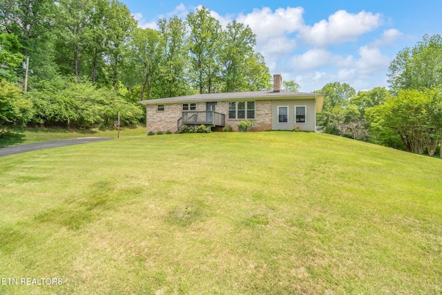 ranch-style home featuring brick siding, a front lawn, a wooden deck, and a chimney