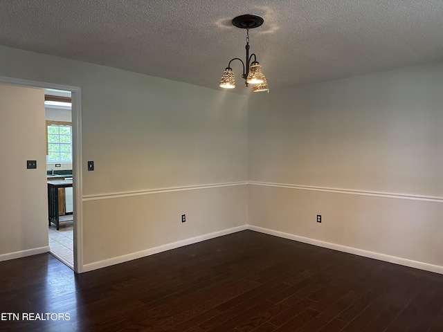 spare room featuring a textured ceiling, baseboards, an inviting chandelier, and wood finished floors