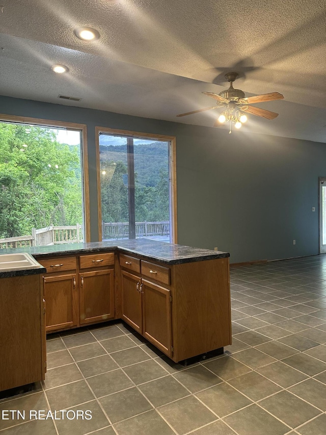 kitchen featuring visible vents, ceiling fan, dark tile patterned floors, a textured ceiling, and brown cabinets