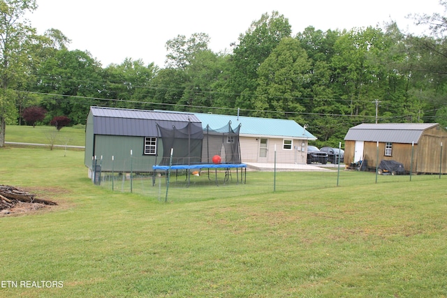 view of yard with an outdoor structure, a trampoline, fence, and a storage unit