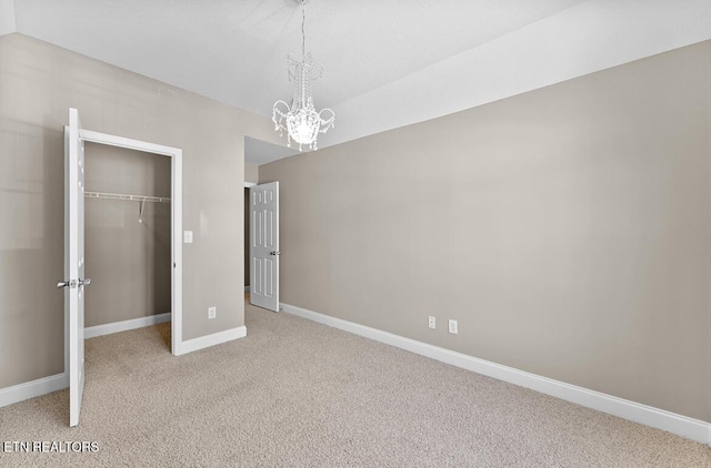 unfurnished bedroom with a walk in closet, a chandelier, carpet, baseboards, and a closet