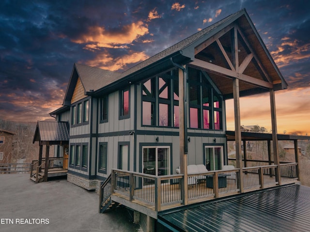back of house at dusk featuring board and batten siding, a patio, roof with shingles, and a balcony