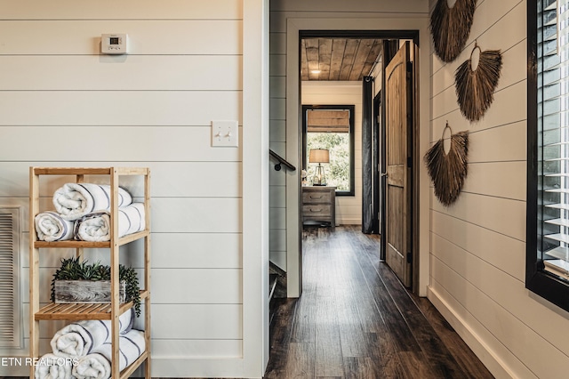 hallway with dark wood finished floors and wooden walls