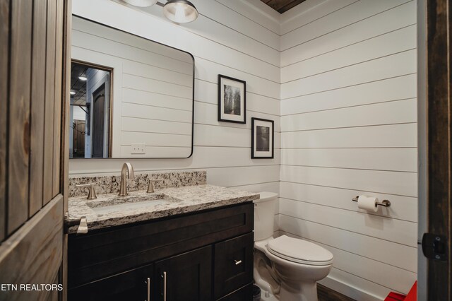 bathroom with toilet, wooden walls, wood finished floors, and vanity