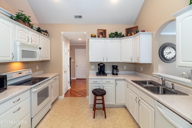 kitchen featuring a sink, white appliances, visible vents, vaulted ceiling, and white cabinets