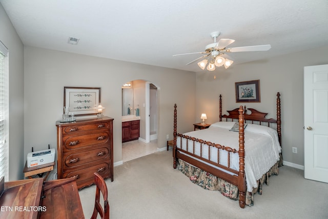 bedroom featuring ensuite bathroom, baseboards, ceiling fan, arched walkways, and light colored carpet