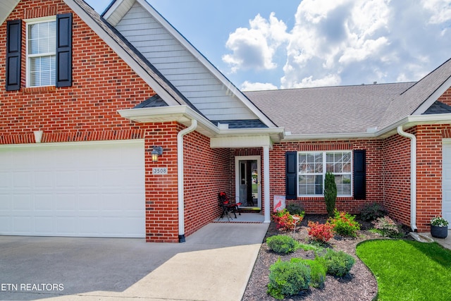 entrance to property featuring concrete driveway, brick siding, and roof with shingles