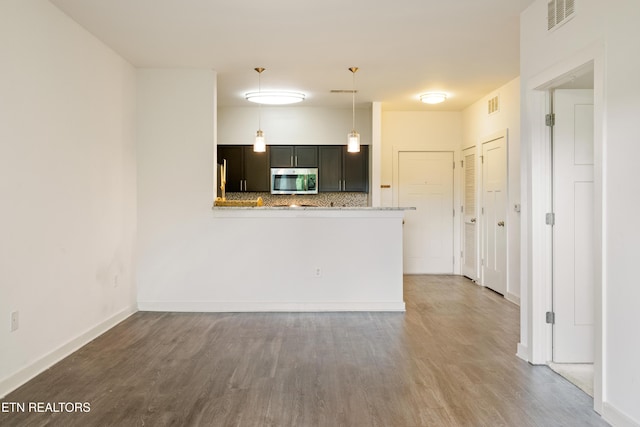 kitchen with stainless steel microwave, tasteful backsplash, wood finished floors, decorative light fixtures, and visible vents