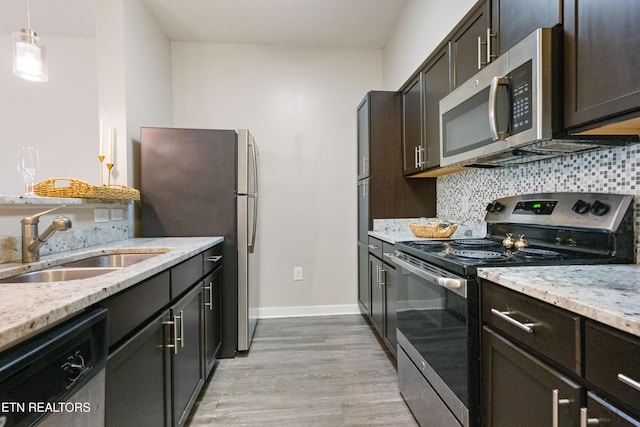 kitchen featuring light wood finished floors, a sink, stainless steel appliances, baseboards, and tasteful backsplash