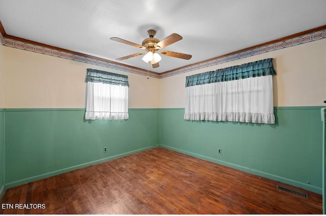spare room featuring a ceiling fan, visible vents, wainscoting, and wood finished floors