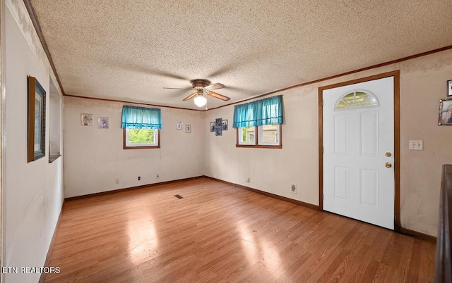empty room featuring a ceiling fan, a textured ceiling, baseboards, light wood-style floors, and ornamental molding