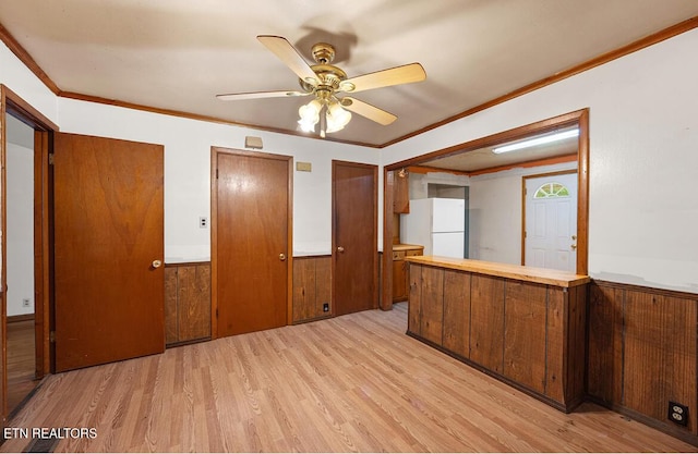 interior space featuring wainscoting, crown molding, a ceiling fan, and light wood finished floors