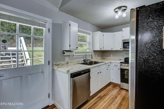 kitchen with white cabinetry, appliances with stainless steel finishes, a sink, and light wood-style floors
