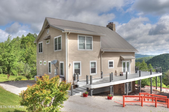 back of property featuring a chimney, metal roof, a deck, a patio area, and cooling unit