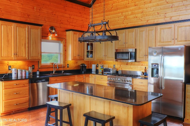 kitchen with appliances with stainless steel finishes, a sink, wooden walls, a breakfast bar area, and a center island