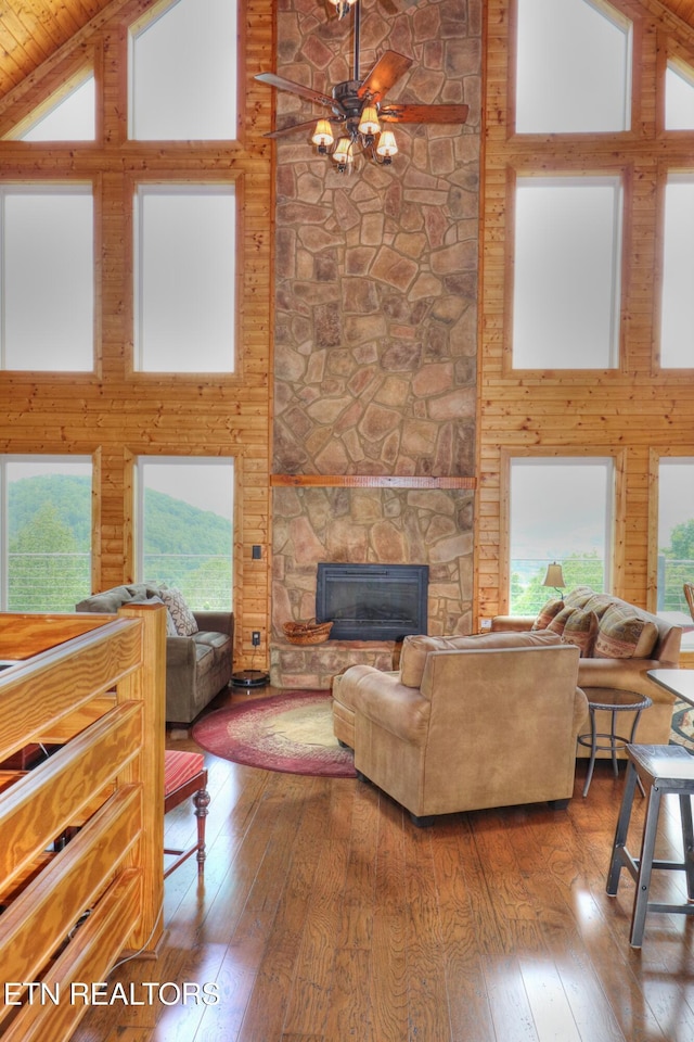 living area with high vaulted ceiling, hardwood / wood-style floors, ceiling fan, and a stone fireplace