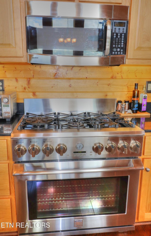 kitchen featuring appliances with stainless steel finishes, dark countertops, light brown cabinetry, and wood walls