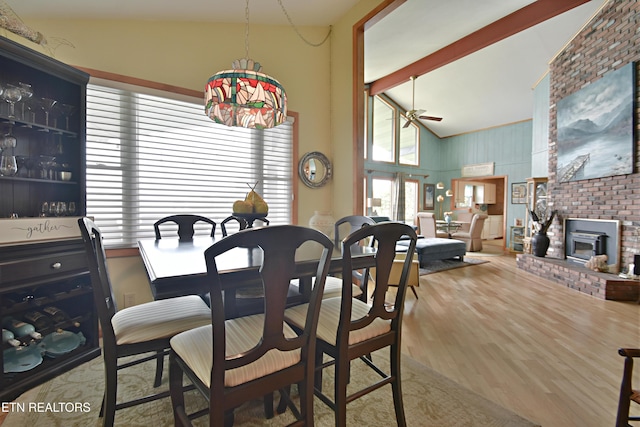 dining space featuring ceiling fan, high vaulted ceiling, wood finished floors, a fireplace, and beam ceiling