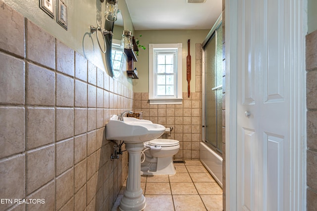 full bath with tile walls, toilet, tile patterned floors, wainscoting, and combined bath / shower with glass door