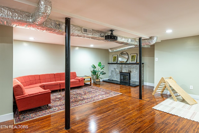 living area with baseboards, visible vents, a fireplace with raised hearth, and wood finished floors