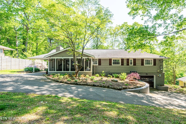 view of front facade with an attached garage, a sunroom, a chimney, fence, and driveway