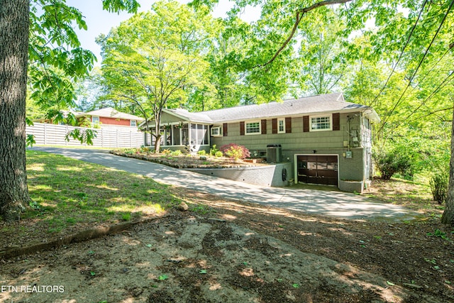 view of front facade featuring an attached garage, a sunroom, fence, concrete driveway, and central AC unit