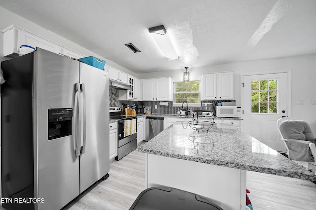 kitchen featuring white cabinetry, stainless steel appliances, under cabinet range hood, and plenty of natural light