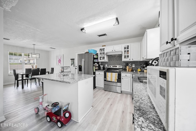 kitchen featuring stainless steel appliances, light wood-type flooring, visible vents, a textured ceiling, and under cabinet range hood