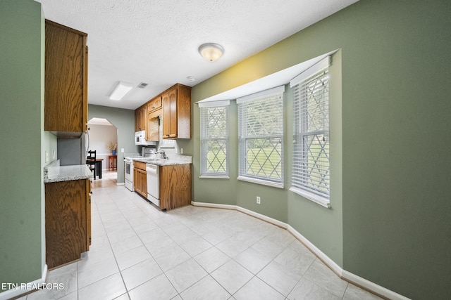 kitchen featuring light tile patterned floors, a sink, baseboards, arched walkways, and white appliances