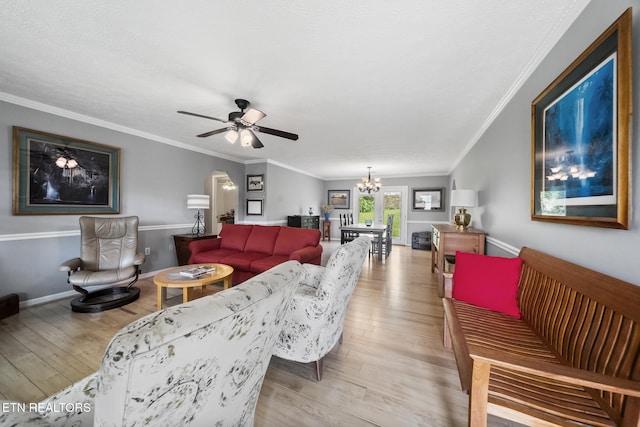 living room featuring light wood-style flooring, ceiling fan with notable chandelier, crown molding, baseboards, and arched walkways