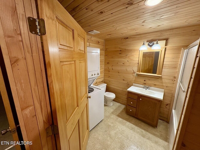bathroom with toilet, vanity, tile patterned floors, wooden walls, and stacked washing maching and dryer