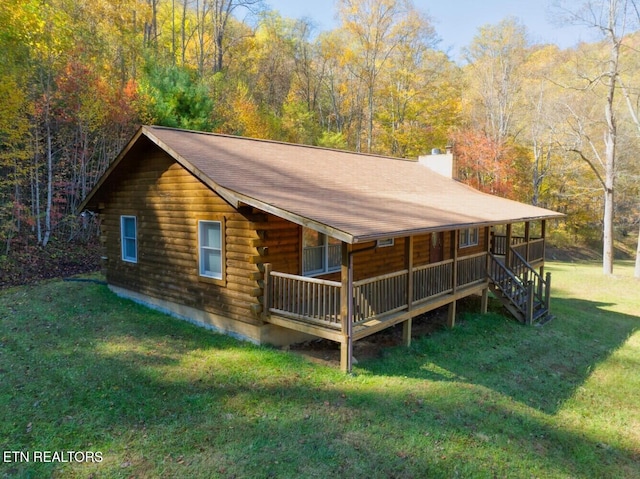 back of house featuring covered porch, a yard, log exterior, a chimney, and a forest view