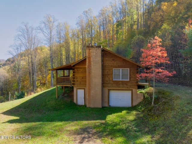 view of home's exterior featuring a wooded view, a chimney, a wooden deck, a lawn, and log exterior