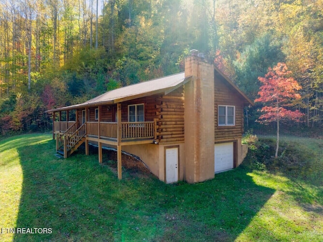 view of front of home featuring a chimney, a wooded view, log siding, a front yard, and a porch