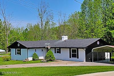 ranch-style house featuring concrete driveway, a chimney, a front yard, and a carport