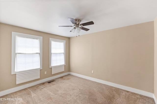 empty room with light colored carpet, baseboards, a ceiling fan, and visible vents
