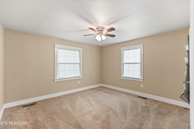 carpeted empty room featuring ceiling fan, plenty of natural light, and visible vents