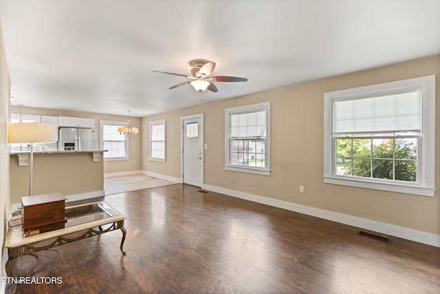 unfurnished living room featuring wood finished floors, visible vents, baseboards, and ceiling fan with notable chandelier