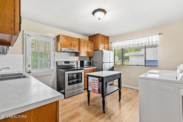 kitchen with washer and clothes dryer, a sink, under cabinet range hood, a wealth of natural light, and appliances with stainless steel finishes