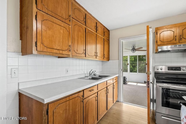 kitchen featuring under cabinet range hood, a sink, electric stove, light countertops, and tasteful backsplash
