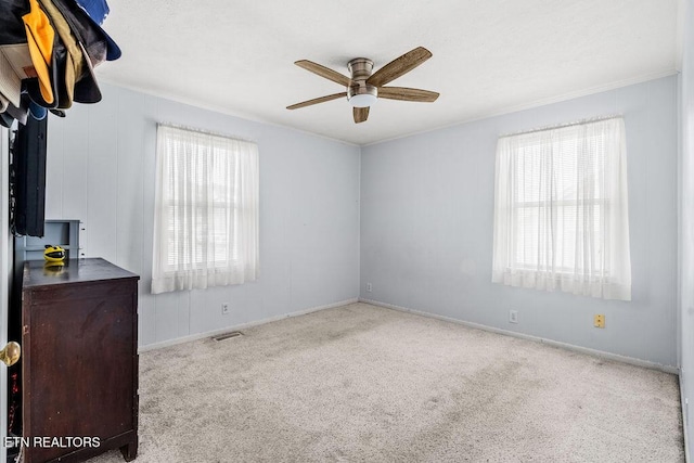 carpeted empty room with a healthy amount of sunlight, crown molding, ceiling fan, and visible vents