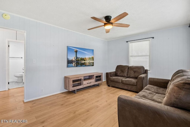 living room featuring ornamental molding, light wood-style floors, ceiling fan, and a textured ceiling