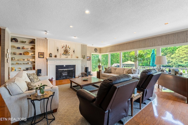 living area featuring a textured ceiling, built in shelves, wood finished floors, and a high end fireplace