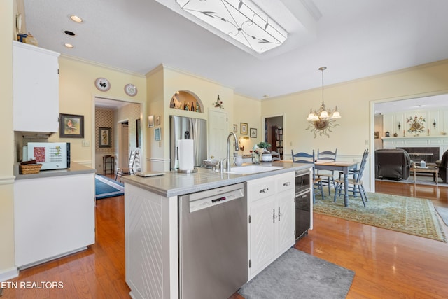 kitchen with a sink, wood finished floors, crown molding, white cabinets, and appliances with stainless steel finishes