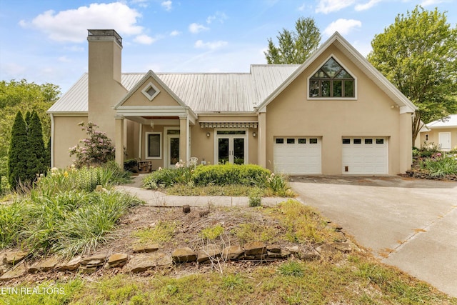 view of front facade featuring concrete driveway, a chimney, stucco siding, metal roof, and french doors