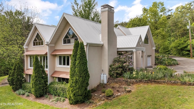 view of home's exterior featuring stucco siding, a chimney, a garage, concrete driveway, and metal roof